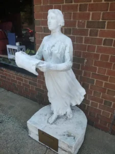 Weathered white statue of a woman holding a scroll, inscribed "Freedom".