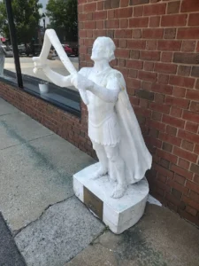 Weathered white statue of a figure wielding a slingshot.