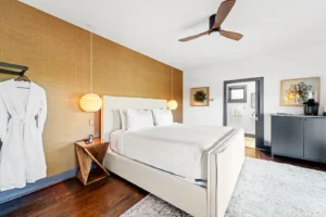 Modern bedroom featuring a white bed, warm accent wall, wooden nightstand.