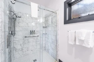 Glass shower with marble tile and window light.