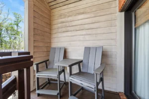 Two wooden chairs and table on a porch with window.