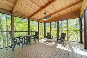 Deep Woods Cottage screened-in porch with wooden beams, table, and forest views.