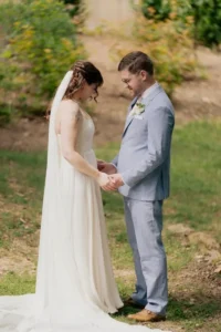 A bride in a flowing white gown and veil holds hands.
