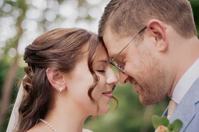 A close-up of a bride and groom's profiles, showcasing elegant wedding attire against a blurred outdoor background.