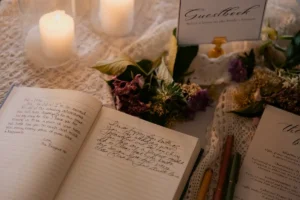 A book opened to a handwritten page, alongside a lit candle, indoors.