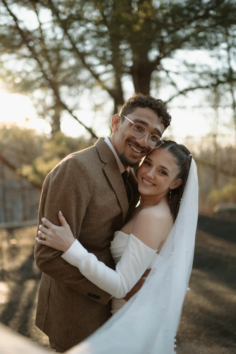A close-up portrait of the bride and groom smiling and embracing outdoors during the "golden hour" sunset.