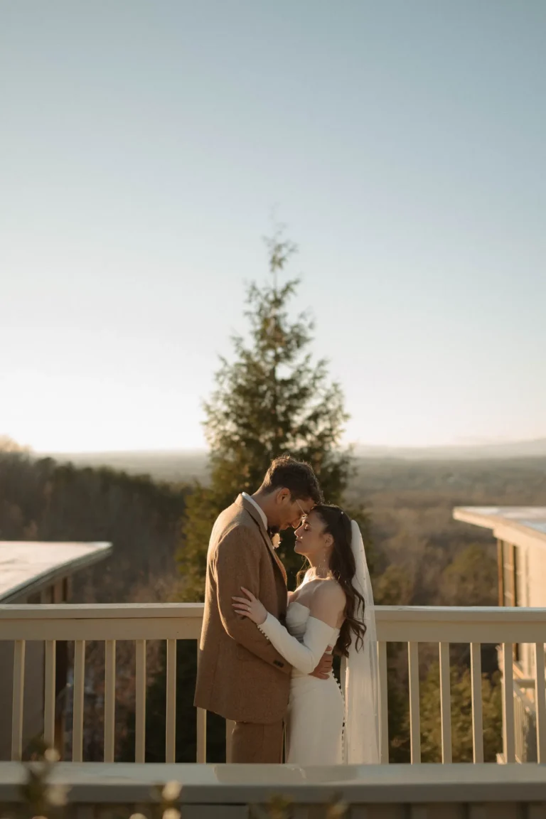 bride and groom sharing a quiet moment on a balcony overlooking a vast, sunlit forest landscape.