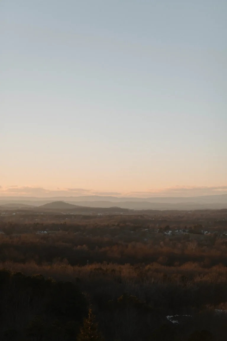 A vertical landscape shot of a rolling valley and distant mountains under a soft, hazy sunset sky.