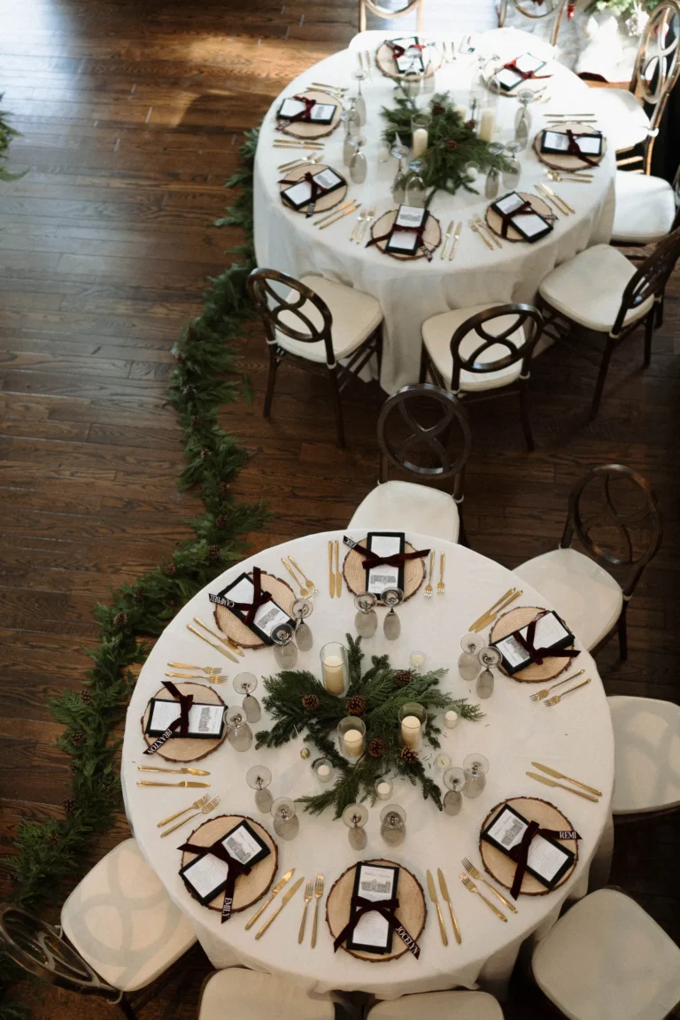 Overhead view of two elegant round reception tables set with white linens and evergreen centerpieces.