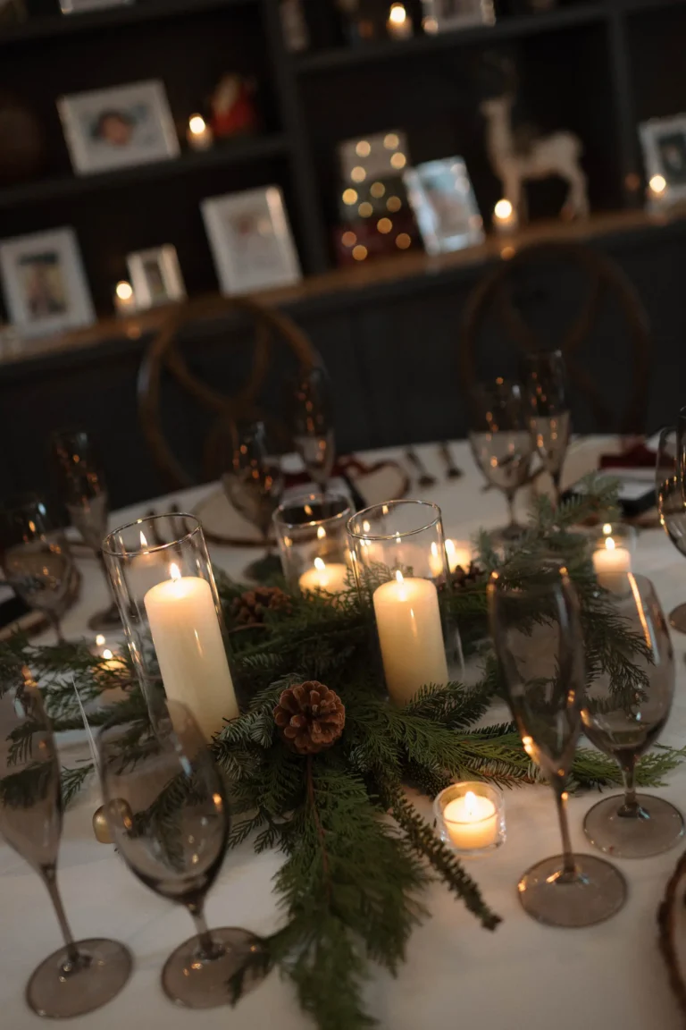 Reception table featuring glowing white candles nestled in pine branches and evergreen needles.