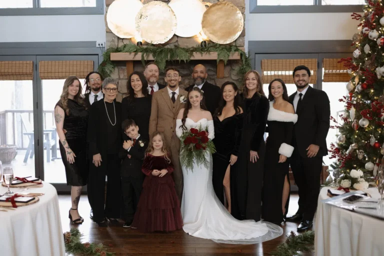 Family posing indoors in front of a fireplace decorated with greenery and a Christmas tree.